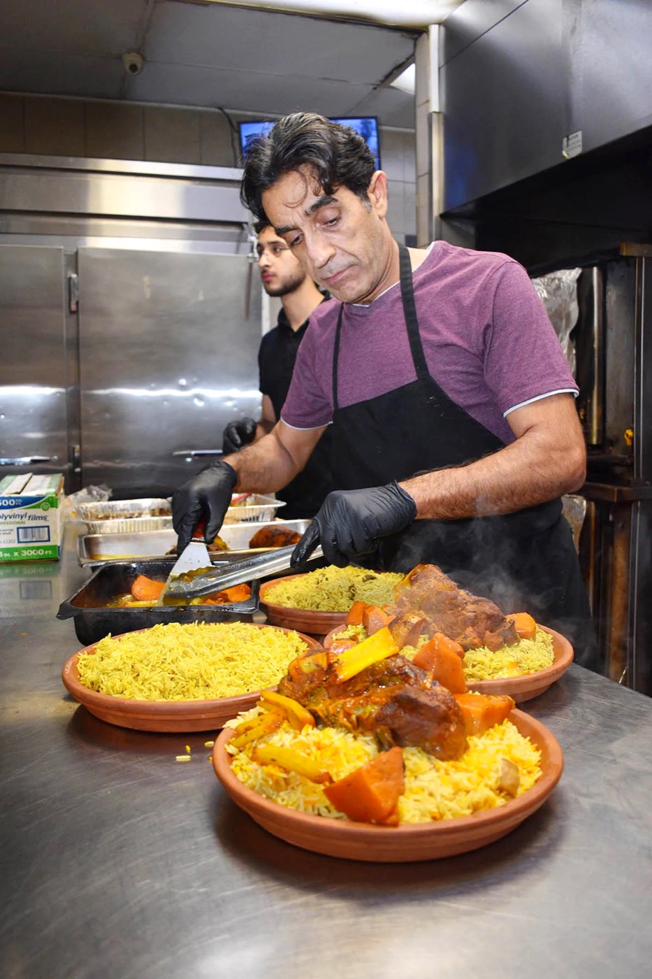 Mohd Mahd plating lamb and saffron rice in the Old School kitchen, one of his sons behind him.