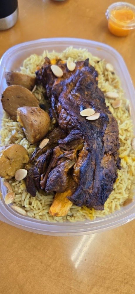 Slow-roasted lamb shoulder resting on saffron rice, scattered with toasted almonds.